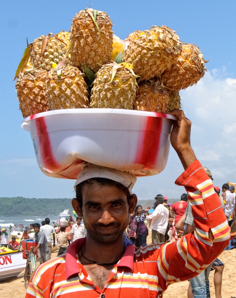 Man holding tub of pineapples on his head, goa india