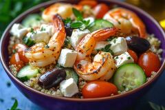 This vibrant bowl features quinoa topped with grilled shrimp, diced cucumbers, cherry tomatoes, black olives, and feta cheese. Fresh herbs and olive oil enhance its flavors in natural light.