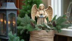 A beautifully crafted angel statue holds a lantern, surrounded by pine branches and cones. This festive arrangement adds warmth and joy to the cozy winter setting.