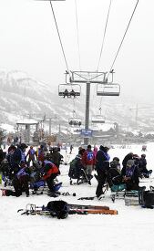 Skiers gather at the base of a chairlift at a busy ski resort