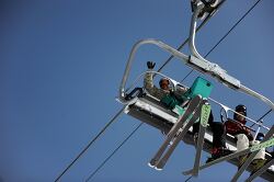 view from below of a ski lift carrying skiers and snowboarders
