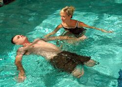 woman assists a man floating on his back in a swimming pool