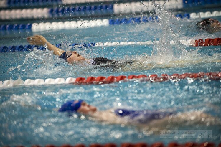 Swimmers racing in a pool, performing backstroke