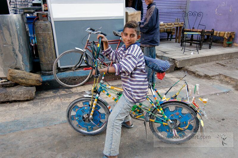 A young boy proudly rides his creatively decorated bicycle along a street in Aswan Egypt Bright colors and unique designs adorn his bike as he navigates the bustling area