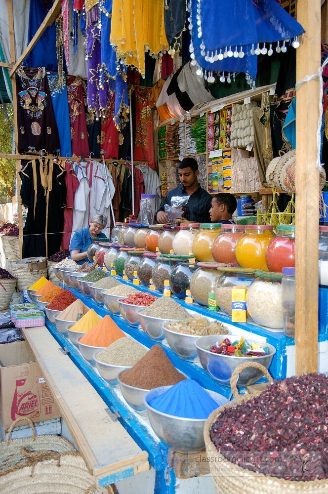 A vibrant market stall showcases an array of spices and herbs in various colors attracting visitors with its rich aromas Two men assist customers enhancing the lively atmosphere