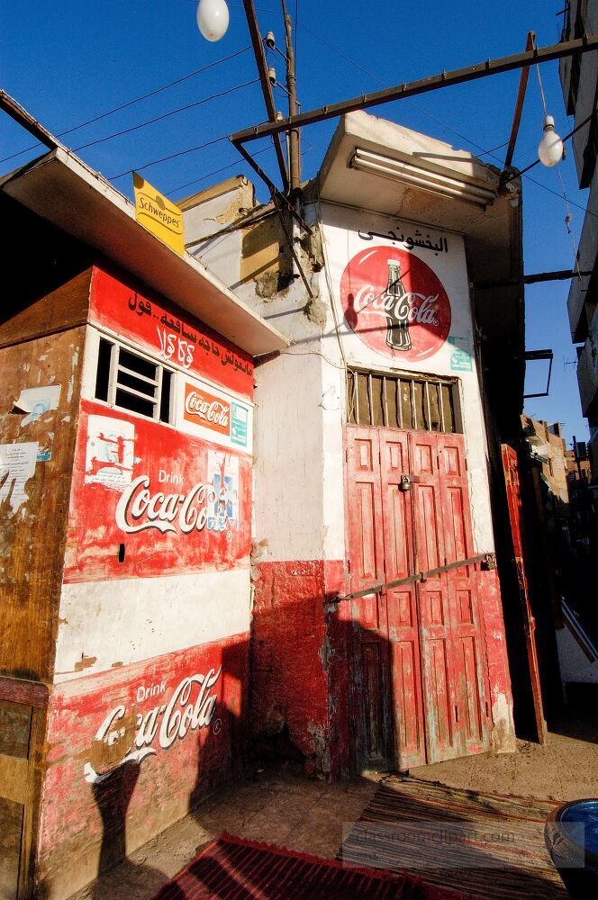 Colorful buildings line the streets of Aswan Egypt featuring a vintage entrance adorned with brand signage Locals engage in daily activities surrounded by vibrant city life