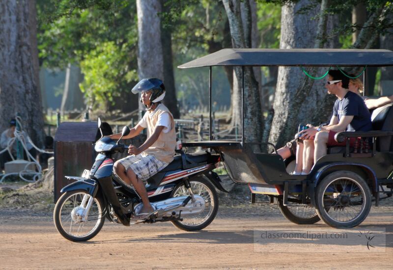 Visitors enjoy a delightful ride through the lush surroundings of Siem Reap Cambodia as they approach the magnificent Angkor Wat. The warm sun illuminates their journey enhanced by vibrant flora.