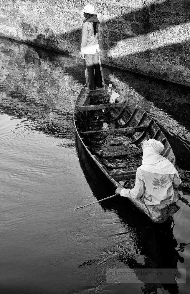 In the tranquil waters of Siem Reap two boatmen navigate their wooden vessel surrounded by the historical ambiance of Angkor Wat. Their focused expressions reflect a deep connection to this serene landscape.