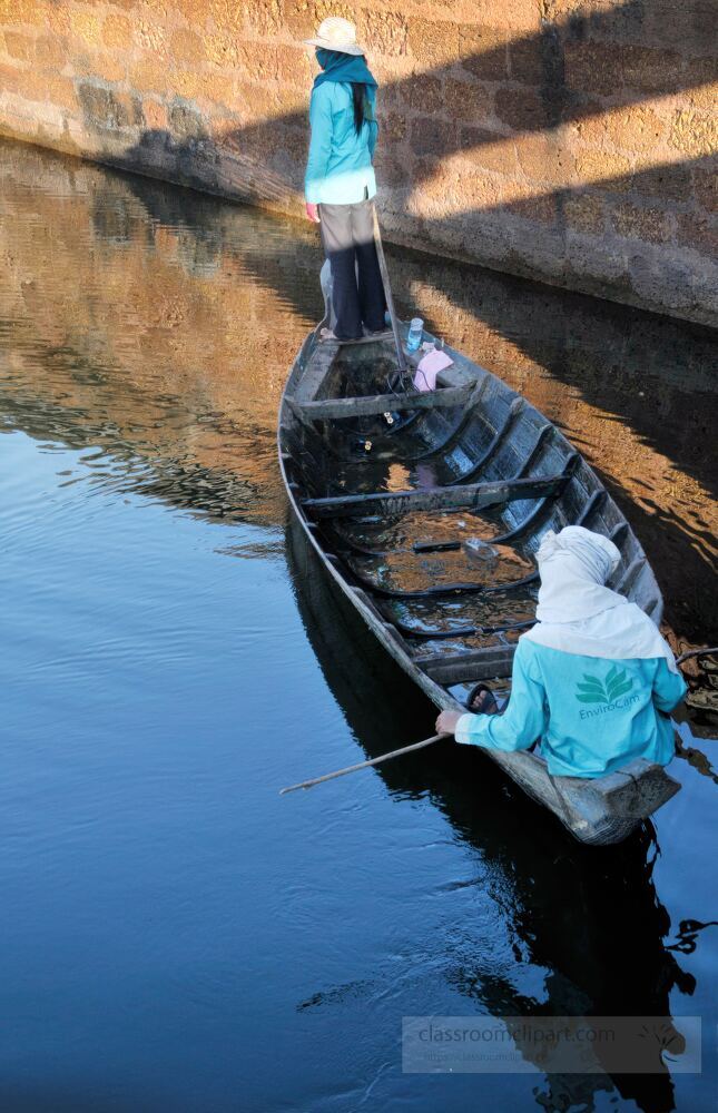 Two figures navigate a peaceful waterway in Siem Reap Cambodia surrounded by the rich history of Angkor Wat. The still water reflects the landscape creating a serene atmosphere at dusk.