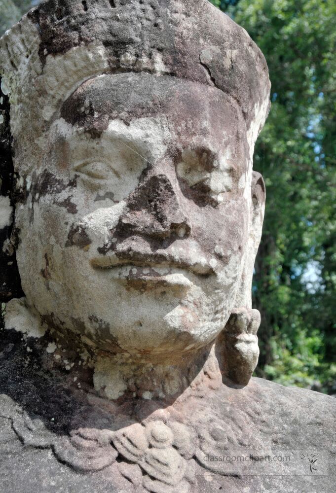 Ancient stone statue adorned with intricate carvings stands proud among the lush greenery of Angkor Wat in Siem Reap. Sunlight casts a soft glow on its weathered features revealing its timeless beauty.