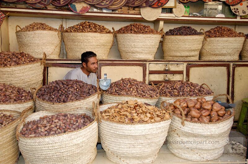 A vendor sits among large woven baskets filled with an assortment of dried fruits in a busy market in Aswan Egypt The vibrant display attracts local shoppers