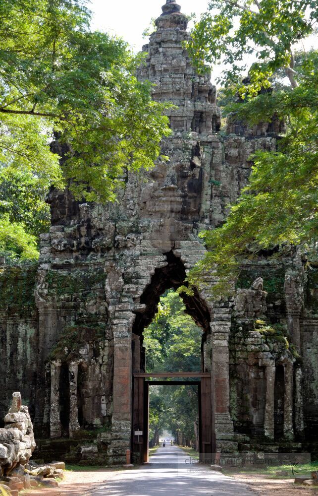 Majestic stone gate stands tall at the entrance of Angkor Wat in Siem Reap Cambodia. Lush trees provide shade as visitors approach the ancient ruins capturing the essence of history and nature in harmony.