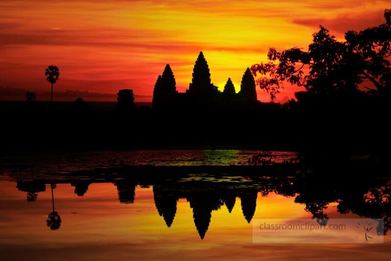 As the sun sets the silhouette of Angkor Wat rises against a vibrant sky casting reflections on the calm waters nearby. This breathtaking view in Siem Reap captures the magic of Cambodia.